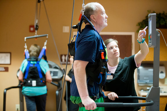 Jim Horrocks, assisted by physical therapist Christine Montes, exercises on a treadmill while wearing a stabilizing harness at Life Care Center of Elkhorn.